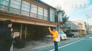 PR動画「佐渡の極」第3弾の一場面。ガイドの笠井正昭さんが趣ある町並みを紹介している