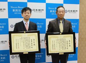 金融知識普及功績者として表彰された栗井英大氏(左)と諏訪部寛栄氏=新潟市中央区