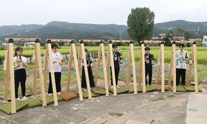 田んぼを背景に酒瓶を使って演奏する明治大の学生たち=南魚沼市五郎丸