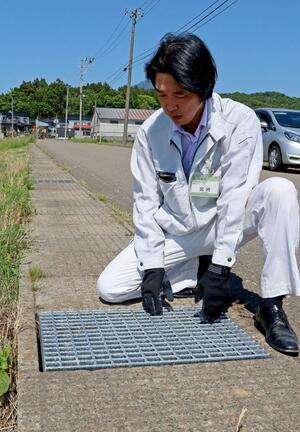 市道の側溝に設置した格子状の鉄製のふたが盗まれ、新たに設置したものを確認する市の職員=上越市柿崎区