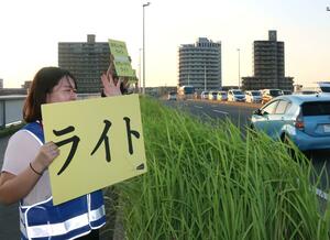 手作りのパネルを掲げ、早めのライト点灯を促すNUTSのメンバー=新潟市中央区の千歳大橋