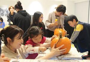 大きなカボチャをくりぬき、ハロウィーンのランタン作りに挑戦する親子連れら=28日、東京・銀座