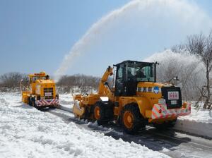 青空に向かって雪を勢いよく飛ばす除雪車＝３日、佐渡市の大佐渡スカイライン
