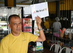 　イスラエル人入店拒否の紙を掲げるポップさん＝２０２５年１２月、タイ・パンガン島（共同）