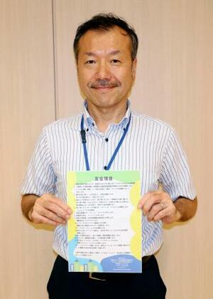 脱炭素に向けた企業宣言制度のチラシを持つ東京都千代田区の川又孝太郎ゼロカーボン推進技監=6月、東京都千代田区