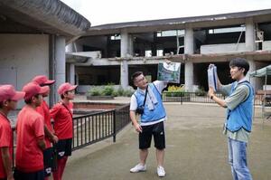 　旧大川小学校を案内する只野哲也さん（右から２人目）と今野憲斗さん（右端）＝２０２４年９月、宮城県石巻市