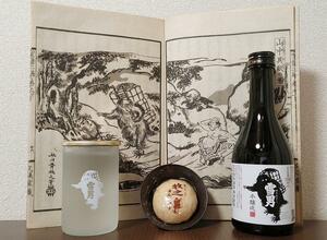 「北越雪譜」に登場する「異獣(いじゅう)」の挿絵を背景に、ゆかりがある南魚沼市塩沢の酒と菓子を置いてみた。左のカップ酒が青木酒造の「雪男」純米酒、右は本醸造。中央は大津商店の「牧之まんじゅう」