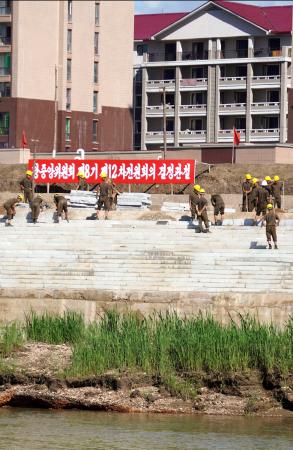北朝鮮北西部の新義州周辺で川沿いの堤防を増築する労働者ら=6日、中国遼寧省丹東から撮影(共同)