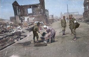 長岡空襲で焼け野原となった市街地で水をくむ人たち。奥に見える塔のある建物は長岡六十九銀行本店(旧北越銀行)=1945年8月3日(長岡戦災資料館所蔵の白黒写真を彩色)