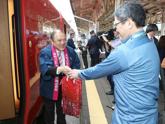 乗客に記念品を手渡すトキ鉄の平井隆志社長（左）＝２３日、上越市の直江津駅