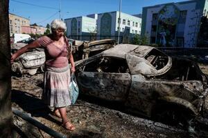 ロシアの攻撃で損壊した車の横を歩く地元女性=4日、ウクライナ・キーウ(AP=共同)