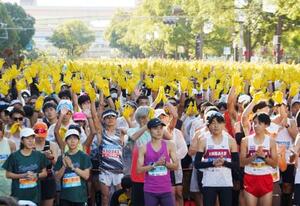 神戸マラソンのスタート前、復興の象徴のヒマワリを表した黄色の手袋を掲げるランナー=16日午前、神戸市中央区