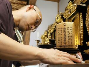 長岡空襲で犠牲になった9少女の名前が記された遺影をきれいにする宝来寺住職の乙川大樹さん=阿賀町豊実