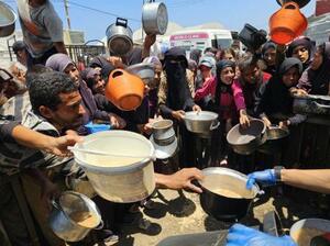 15日、ガザ南部ハンユニス西方マワシ地区で、援助団体が配る温かい食べ物を受け取ろうとするパレスチナ人(ゲッティ=共同)