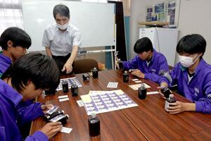 あおき味噌の青木光達社長の助言を受けながら、クラフトコーラのラベルを貼る三和中の生徒=上越市三和区島倉