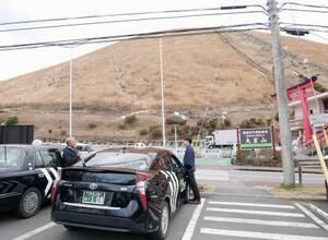 　観光名所「大室山」の近くで利用客を待つタクシー運転手＝１２日、静岡県伊東市
