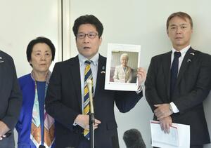 羽田空港で、横田早紀江さんの写真を手にして取材に応じる拉致被害者家族会代表の拓也さん(中央)。右は事務局長の飯塚耕一郎さん=5月4日午後
