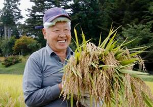 福島県飯舘村長泥地区で稲を刈り、笑顔を見せる庄司喜一さん=24日午前