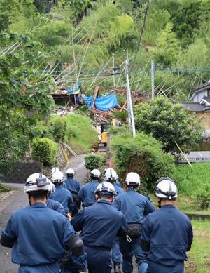 大雨で土砂が流入し倒壊した住宅(奥)に向かう警察官ら=10日午前、鹿児島県姶良市