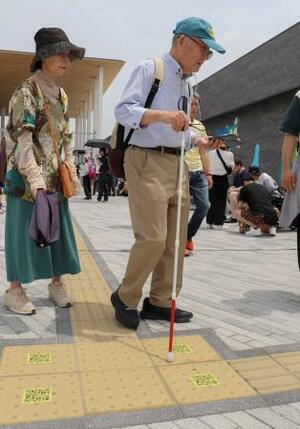 音声で目的地に誘導するスマートフォンアプリ「シカイ」を利用する大久保貫太郎さん(右)=5月、大阪市此花区の夢洲