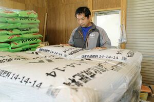 倉庫に置いた肥料を見つめる農家男性。「肥料高は経営に直結する。本当に困る」と嘆く=村上市
