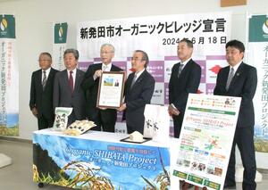 「オーガニックビレッジ宣言」の宣言書を掲げる二階堂馨市長(左から3人目)と花角英世知事(同4人目)ら=6月18日、新発田市住田