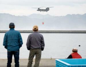地元の漁業関係者が見守る中、山林火災の消火活動のため、海水をくみ上げるヘリコプター=28日午前、岩手県大槌町