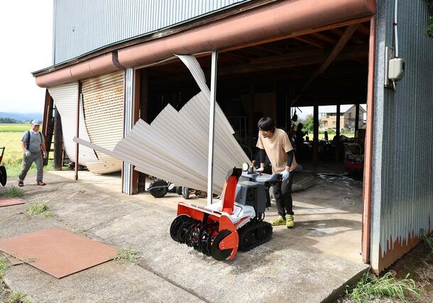 突風でシャッターや壁が壊れた倉庫から商品を取り出す人たち＝１１日、上越市三和区島倉