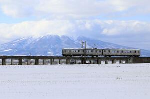 雪が積もった田園地帯を走る弘南鉄道の列車=1月、青森県平川市