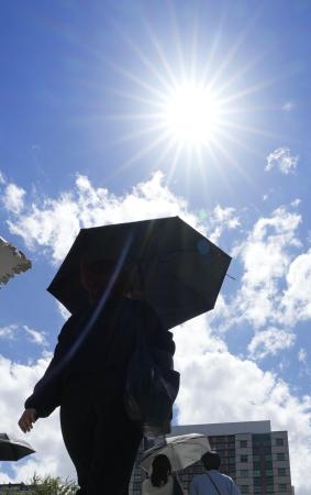 　照りつける夏の日差しの下を歩く人＝２０２４年７月