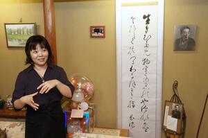 山田花作直筆の書や写真が飾られた店内で話す山田ゆみさん=10日、新潟市西区小針