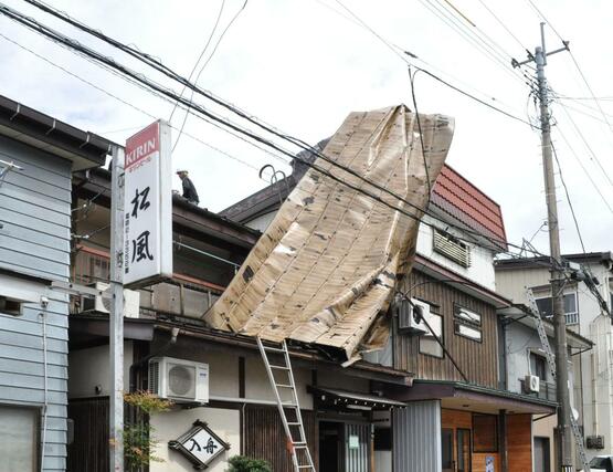 突風で飛ばされ、隣の店舗の屋根に引っかかったトタン屋根＝１１日、魚沼市小出島