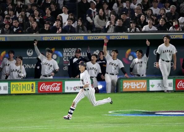 ８回、３ランを放ち一塁へ向かう周東。奥はベンチで盛り上がる日本の選手たち＝東京ドーム