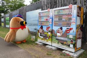 福島潟をPRするデザインのラッピング自動販売機とマスコットキャラクターのクイクイ=新潟市北区