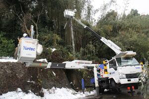 雪の影響で先端が折れた電柱の撤去や電線の張り直しに当たる作業員=2022年12月22日、佐渡市