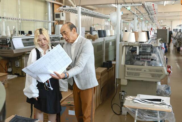 ウメダニットの工場で説明を受けるニットアーティストの蓮沼千紘さん（左）＝５月１４日、五泉市