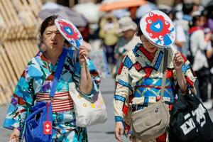 厳しい暑さとなった大阪・関西万博の会場で、うちわで日差しを避けながら歩く人たち=26日午後、大阪市此花区の夢洲