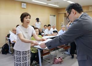 県の担当者に要望書を手渡す「私学の公費助成をすすめる会」の中村直美会長(左)=7日、県庁