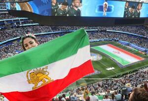 イラン―ニュージーランド戦でピッチに広げられたイラン国旗に抗議し、イラン革命前の旗を掲げるイラン系米国人の女性=15日、ロサンゼルス(共同)