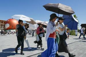厳しい暑さの大阪・関西万博の会場で、日傘を差して歩く人たち=7月、大阪市此花区の夢洲