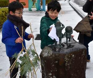 　「水木しげるロード」にある妖怪などのブロンズ像にしめ飾りを取り付ける子どもたち＝２６日、鳥取県境港市