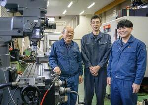　オオツカの工場内で独特の存在感を放つ縦型フライス盤。脇に立つのは（左から）社長の大塚美智夫と社員の大橋徹、古沢達哉だ＝２０２６年３月、茨城県つくば市