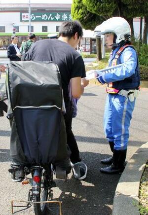 自転車利用者に注意喚起のチラシを配る警視庁の警察官=6月、東京都葛飾区