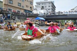 「松川タライ乗り競走」で、水しぶきを上げながら川を下る出場者=6日午前、静岡県伊東市