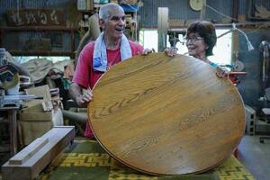 製作したちゃぶ台を手にするダニー・ネフセタイと妻の吉川かほる。ダニーは、みんなが等間隔で座れるちゃぶ台の「和」の思想にほれ込んだ=2025年7月、埼玉県皆野町の工房「ナガリ家」(撮影・堀誠)