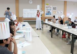 子どもたちに味覚に関する授業をする岸義明さん。「トック」と呼ばれる帽子を児童にも贈った=佐渡市畑野