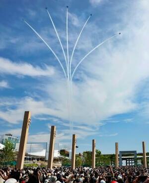 薄雲がかかった大阪・関西万博会場の上空を展示飛行する航空自衛隊のアクロバットチーム「ブルーインパルス」。大勢の来場者が妙技を見守り大きな歓声や拍手が沸いた=12日午後、大阪市此花区の夢洲