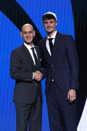 ドラフト会議でマーベリックスから全体1位指名を受け、NBAのシルバー・コミッショナー(左)と握手するデューク大のフラッグ=25日、ニューヨーク(ゲッティ=共同)