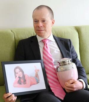 オーストラリア・メルボルン郊外の自宅で、娘のオリビアさんの遺影と骨つぼを手にするロブ・エバンズさん=11月(共同)