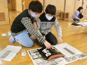 長屋門再生用の瓦にメッセージを書く月岡小６年生＝三条市